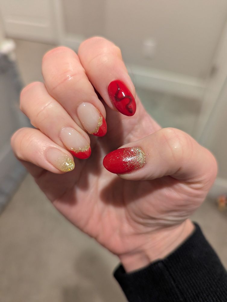Manicured nails with red and gold design. Pointer finger has a snake drawing.