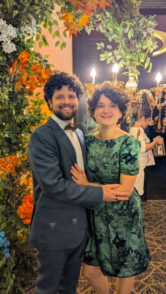 Young couple dressing up - he in black and white suit, she in green and black dress.