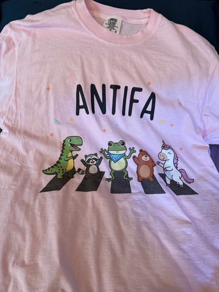Pink t-shirt with cartoon characters and the word ANTIFA.
