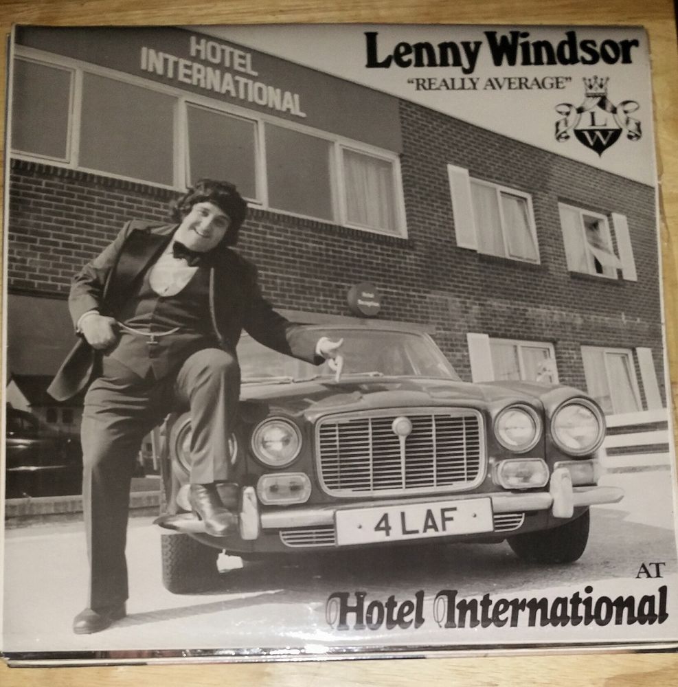 Photograph of the black & white photo album cover for Lenny Windsor "Really Average" At Hotel International, featuring a portly Lenny -  in a 70's 3pc dj suit a with massive lapels, a large bowtie & a fob watch & chain strung between the waistcoat jackets - one foot up on the side bumper of a (i think) Jag with the number playe 4 LAF, all in front of a long flat-roofed 2storey brick building with a number of large windows & the words Hotel International in white letting. 