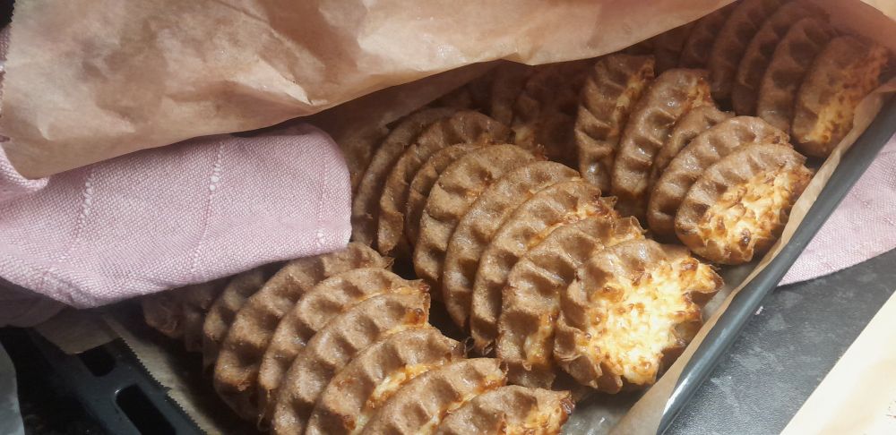 UuniPellin kulma, jossa näkyy suorissa riveissä valmiita karjalanPiirakoita pilkistämässä vaaleanPunaisen leivinLiinan ja leivinPaperin alta.