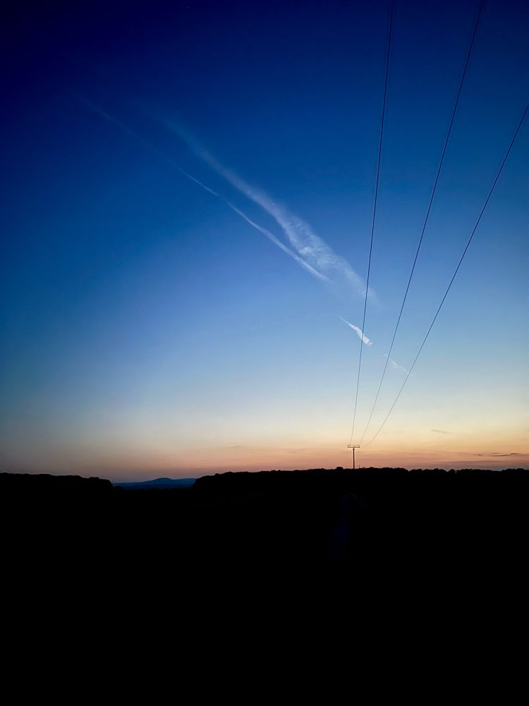 Photo of beginning night, everything is dark except the sky, where the remnants of the day still linger.
The foreground is dominated by power lines.