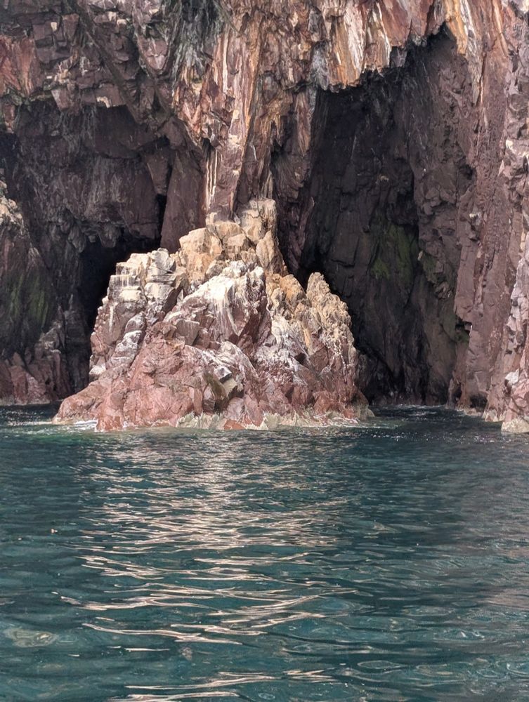 A cave of red and black rock with a central pillar covered in bird shit