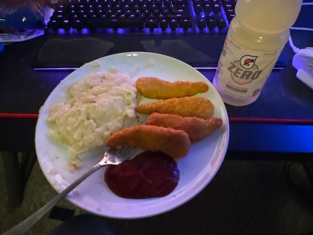 A plate of chicken tenders with ketchup and mashed potatoes next to a yellow Gatorade zero
