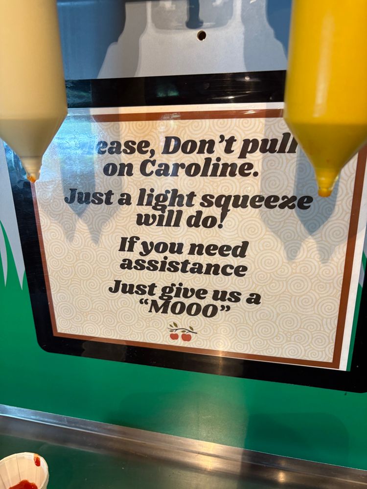 The sign posted below the condiment cow, which reads: "Please don't pull on Caroline. Just a light squeeze will do! If you need assistance, just give us a moo"