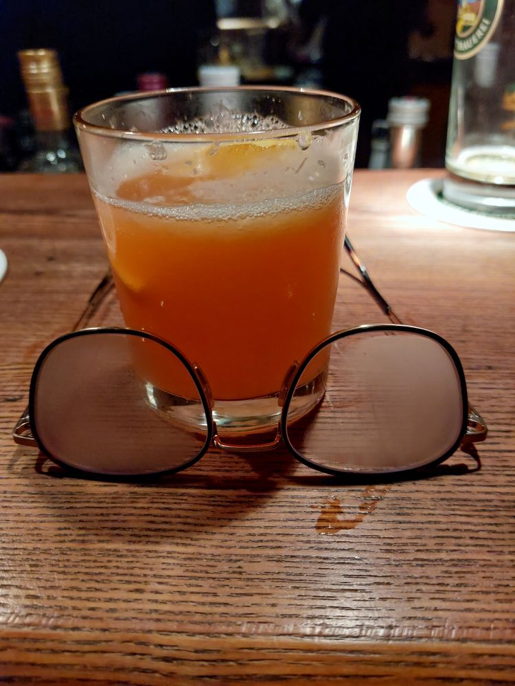 Aperol Sour mit beschlagener Brille vor dem Glas auf Holztresen