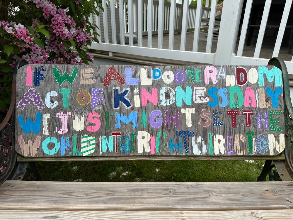 The words “if we all do one random act of kindness daily we just might set the world in the right direction” are painted onto a bench. 