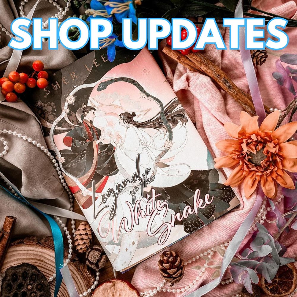 A photo of the Rainbow Crate edition of Legend of the White Snake by Sher Lee. The books sits on top of gray and pink fabric which is draped underneath the book. Various accessories decorate the photo including pearls, pinecones, flowers, sticks and ribbon. Text at the top reads “Shop Updates” in white text with a blue outline. 