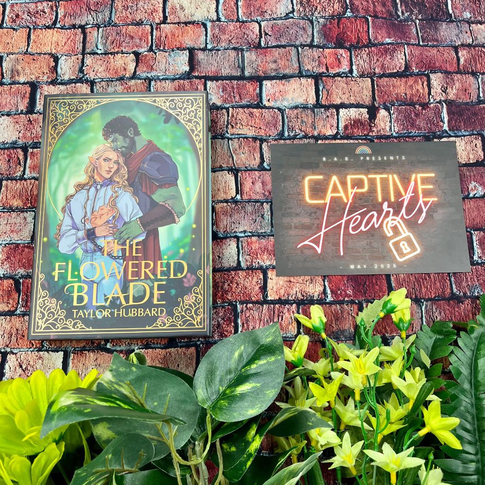 Close up of the front cover of The Flowered Blade and the spoiler card. Underneath them sit various green flowers and leaves. Everything lies on a red brick background.
