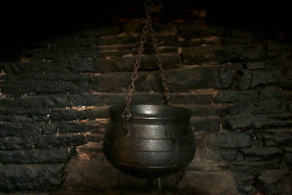 A cast iron cooking pot by a smoke blackened wall, such that might be used by a witch on Halloween