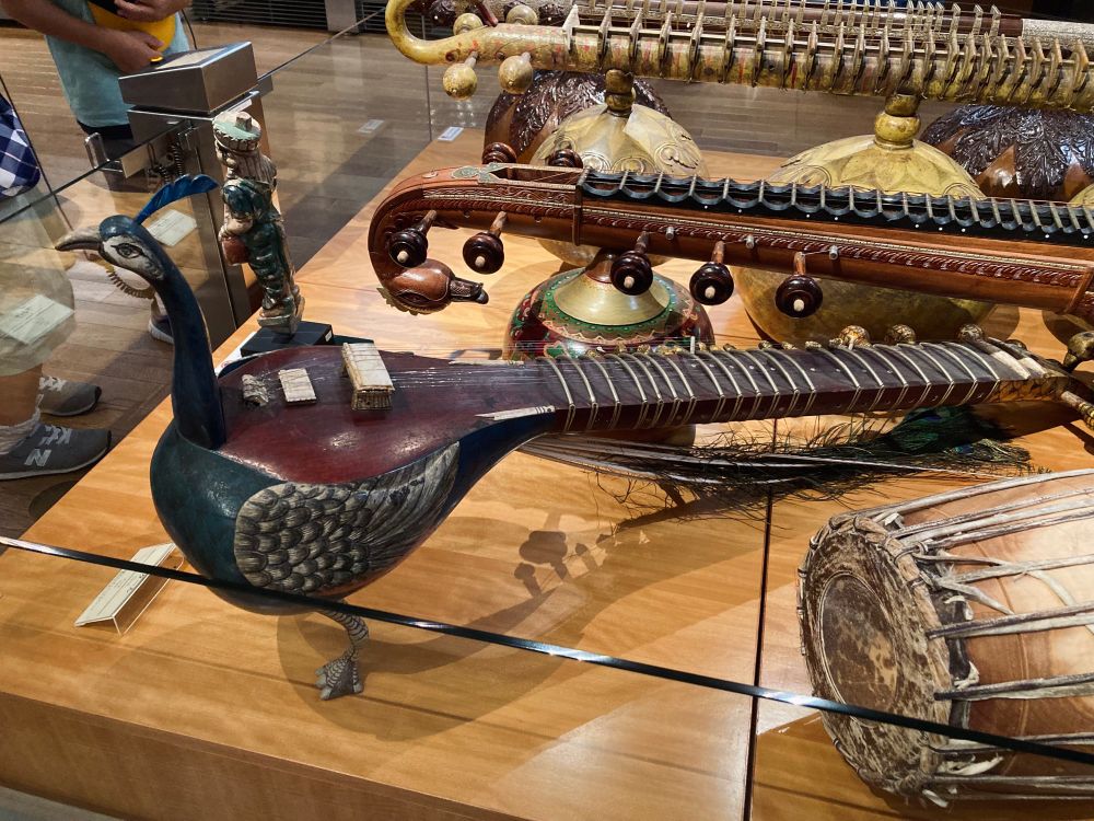 立体的な孔雀の形のシタールの写真。胴体を孔雀の身体、弦の張られた部分を尾に見立て、胴に孔雀の首と足がついて自立している。本物の尾羽もついている