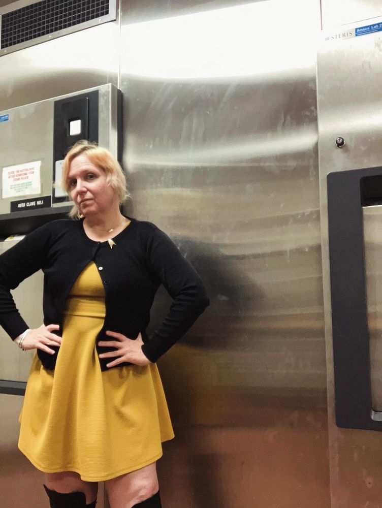 Anika in the style of Star Trek (2009), wearing a gold mini dress with a black cardigan and small Trek delta at the collar, and over the knee black boots. 