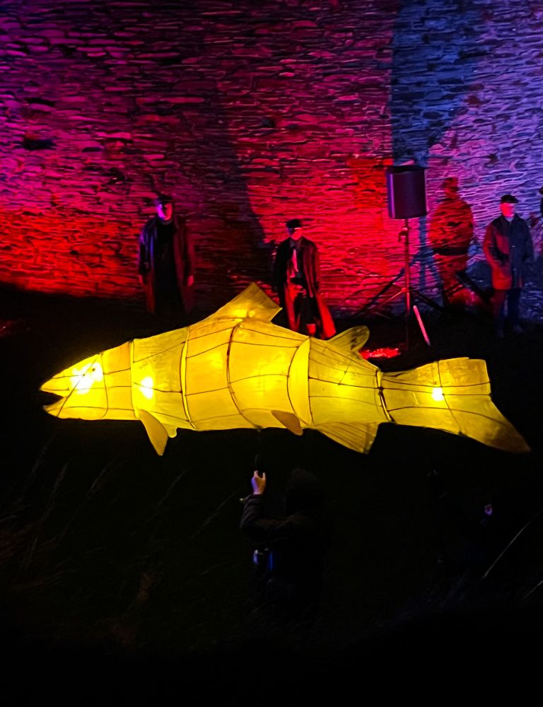 A yellow puppet salmon with internal lighting at a performance of the Phantom Coracle at Cilgerran Castle, Wales. 