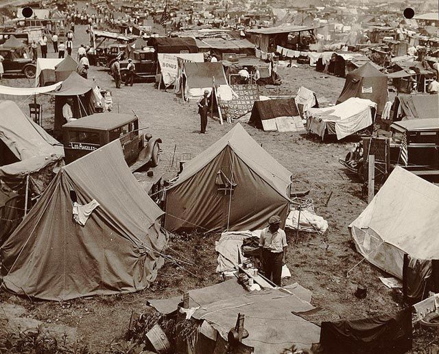 Tents, a few cars, people walking. Sepia photo.