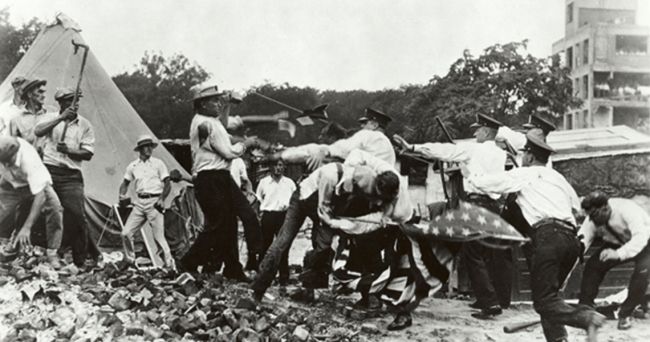Black and white photo of men fighting with police, American flag is sideways, tent in background