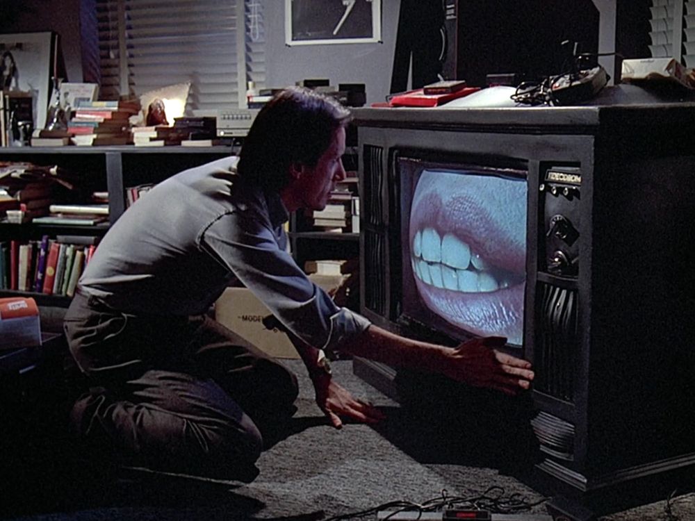 James Woods in Videodrome, kneeling down in his book-filled living room, caressing a large, old-fashioned looking TV showing a giant pair of female lips.