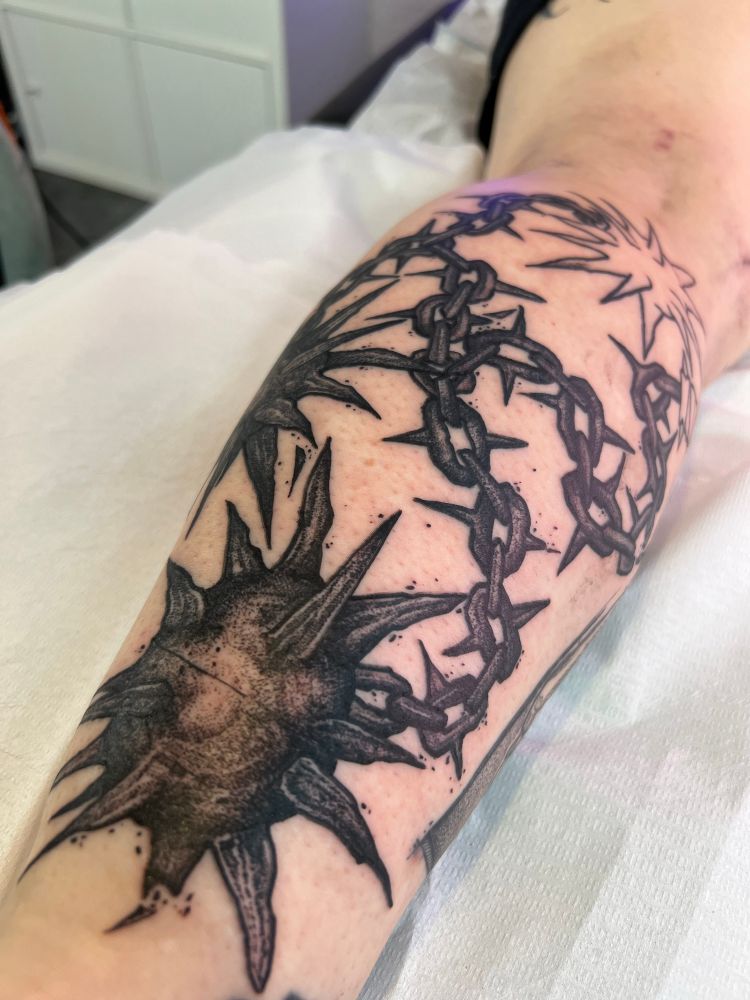 Photo d’un fléau tatoué sur un arrière de mollet.
Il n’est pas encore terminé et est réalisé en fatline et est très sombre dans sa réalisation.
La photo est prise sur fond blanc.
