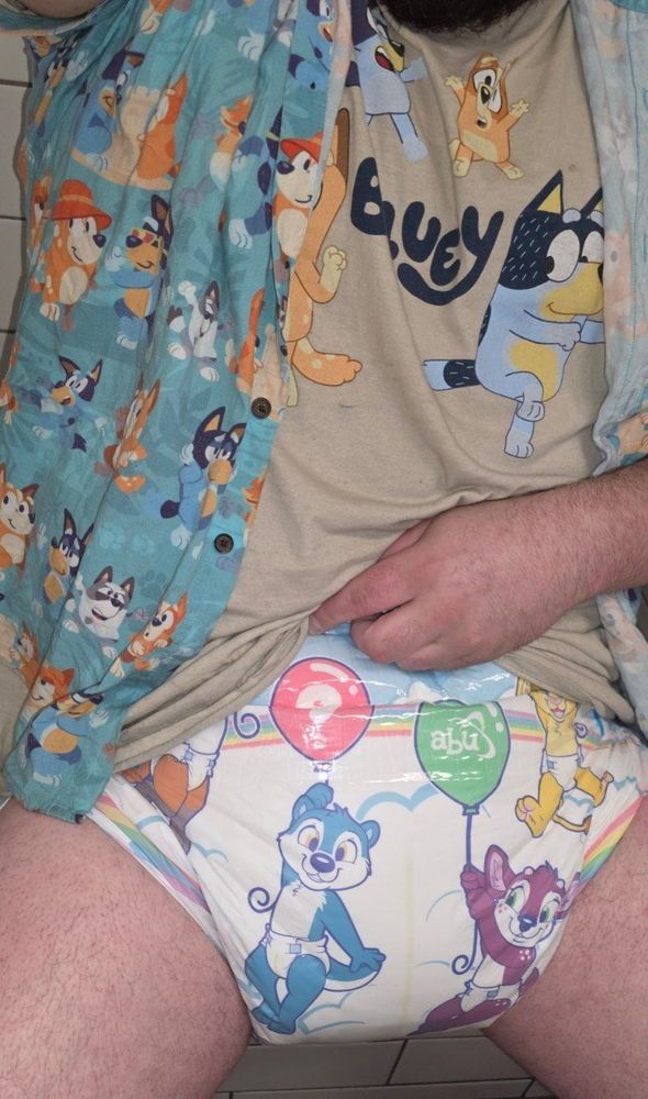 Real life Sylven sitting down, lifting one of their Bluey shirts up to reveal a dry (allegedly) ABUniverse Tiny Tails