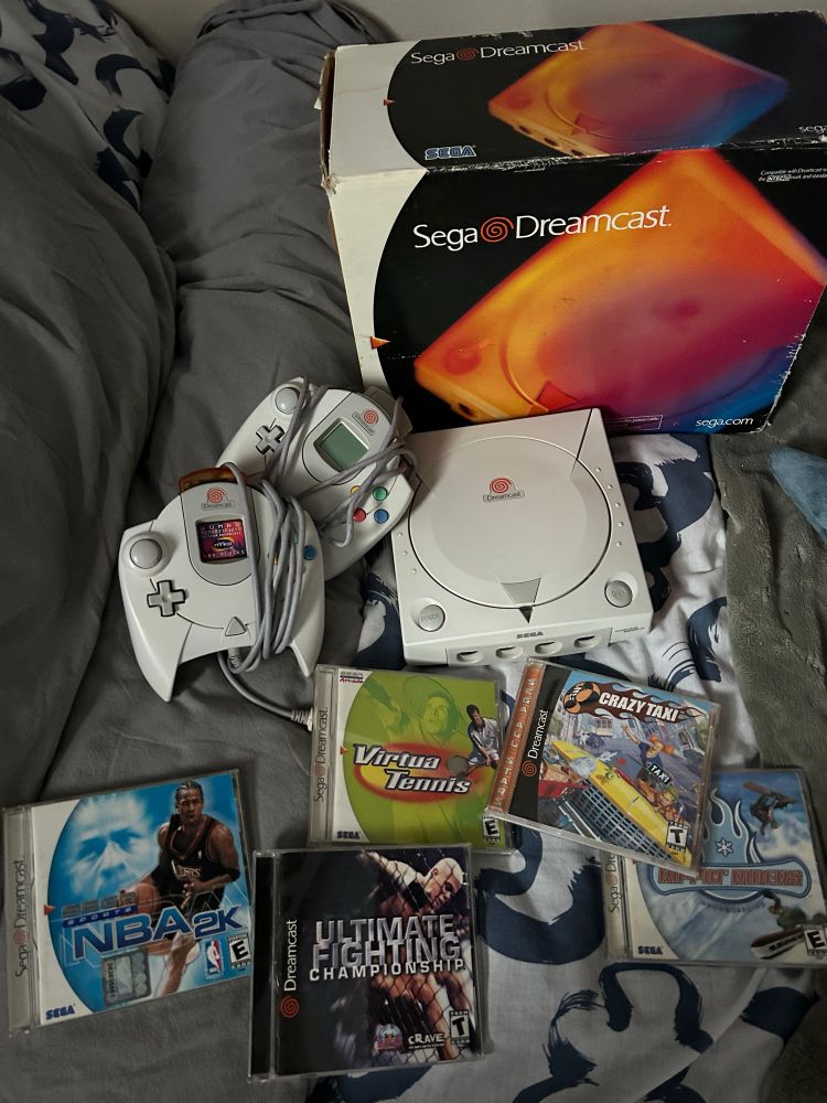 A Sega Dreamcast surrounded by a small stack of games, controllers and its original box. 