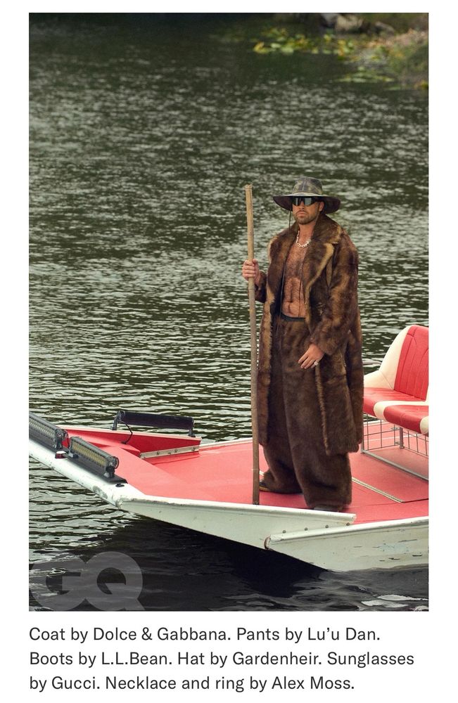 Travis Kielce stands on a boat deck with loads of fur on, a hat, protective eyewear, and no shirt.