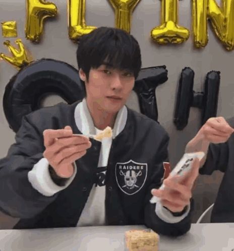 a man wearing a raiders jacket is eating a piece of food