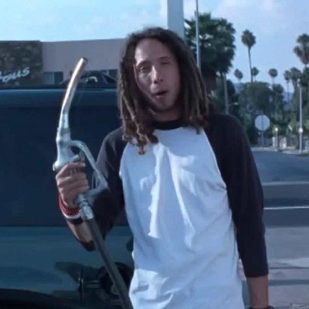 a man with dreadlocks is holding a gas pump in front of a building that says ' focus ' on it