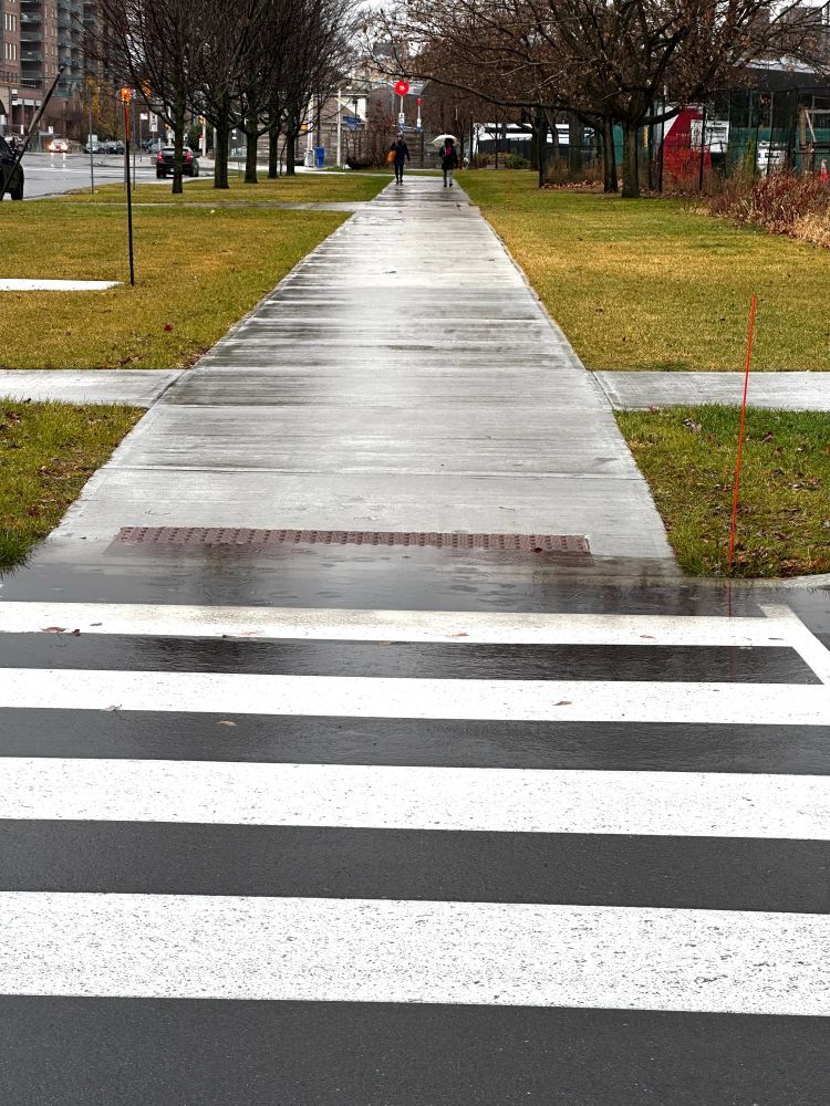 A photo of a crosswalk with a large puddle where the road and the sidewalk meet