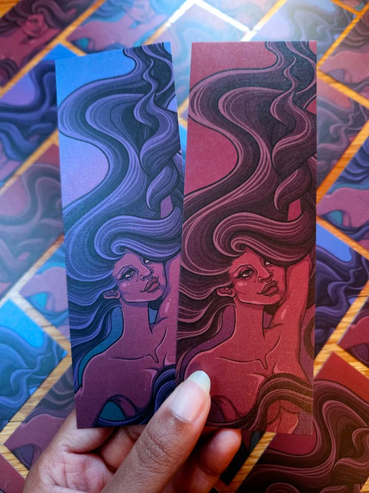 A photo of two bookmarks. They both have a woman reaching upwards while her hair flows up and around her arm. One is a cool color palette while the other is warm. 