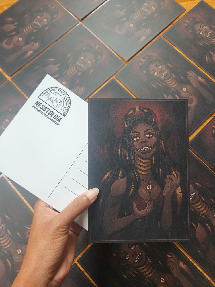 A photo of an art prints. It depicts my "The Darkness" artwork of a Monster like woman with sharp teeth and eyes within her dark hair. The back is a postcard.