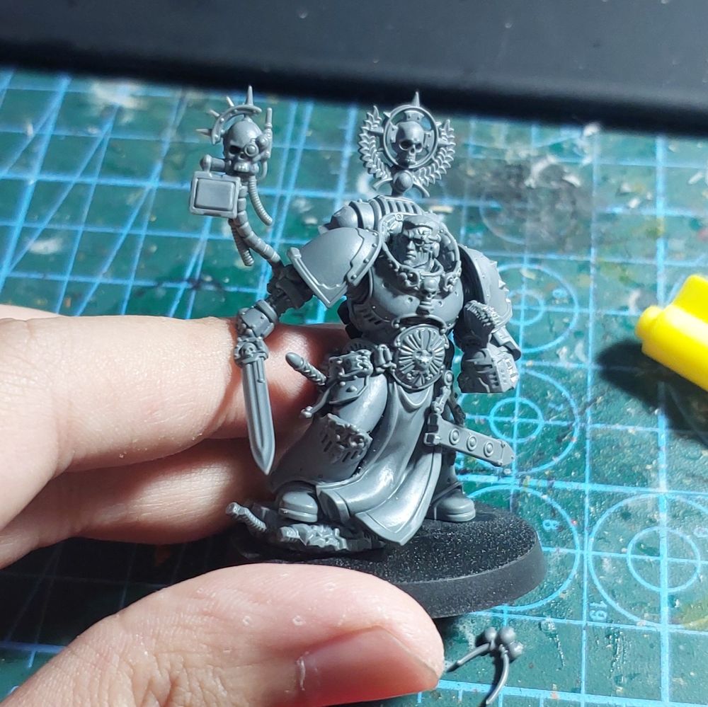 An unpainted space marine miniature wielding a sword and carrying his helmet