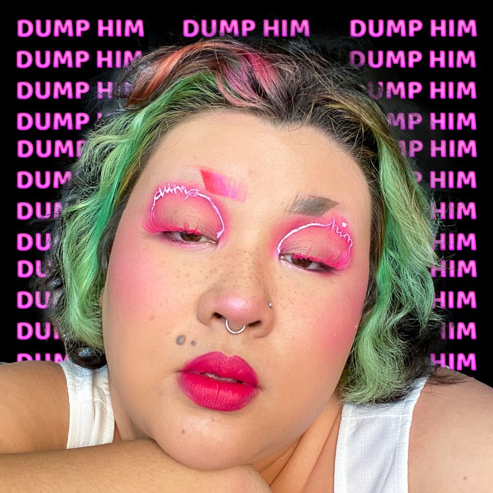 A selfie of Clore resting their chin on their hand. Their facial expression is neutral. Their photo is in front of a black background with repeated pink text that reads “Dump Him”.  They have pink neon eyeliner that reads “Dump Him.”
