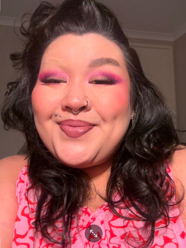 A selfie of Clore with a pink and purple winged smokey eye and iridescent pink inner corner and lid. There is a hot neon pink heart outline in the wing. They are smiling