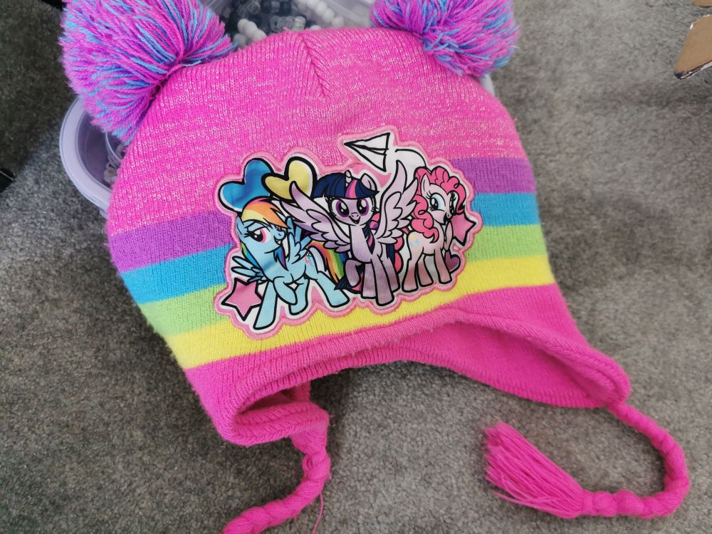 A My Little Pony beanie with Rainbow Dash, Twilight Sparkle and Pinkie pie on it. It's pink with purple, blue, green and yellow stripes going down the middle, and it has 2 blue and purple pom poms and 2 pink tassels on the bottom. 