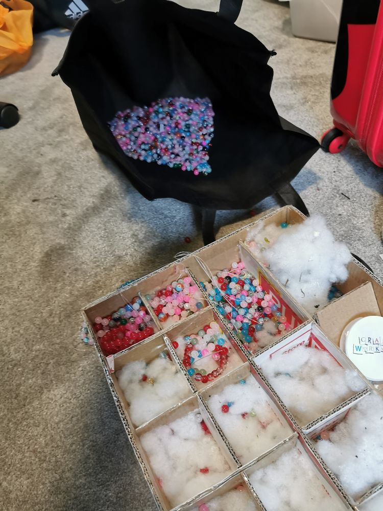A reusable grocery bag and a cardboard box full of multi-coloured beads with all of the colours mixed together 