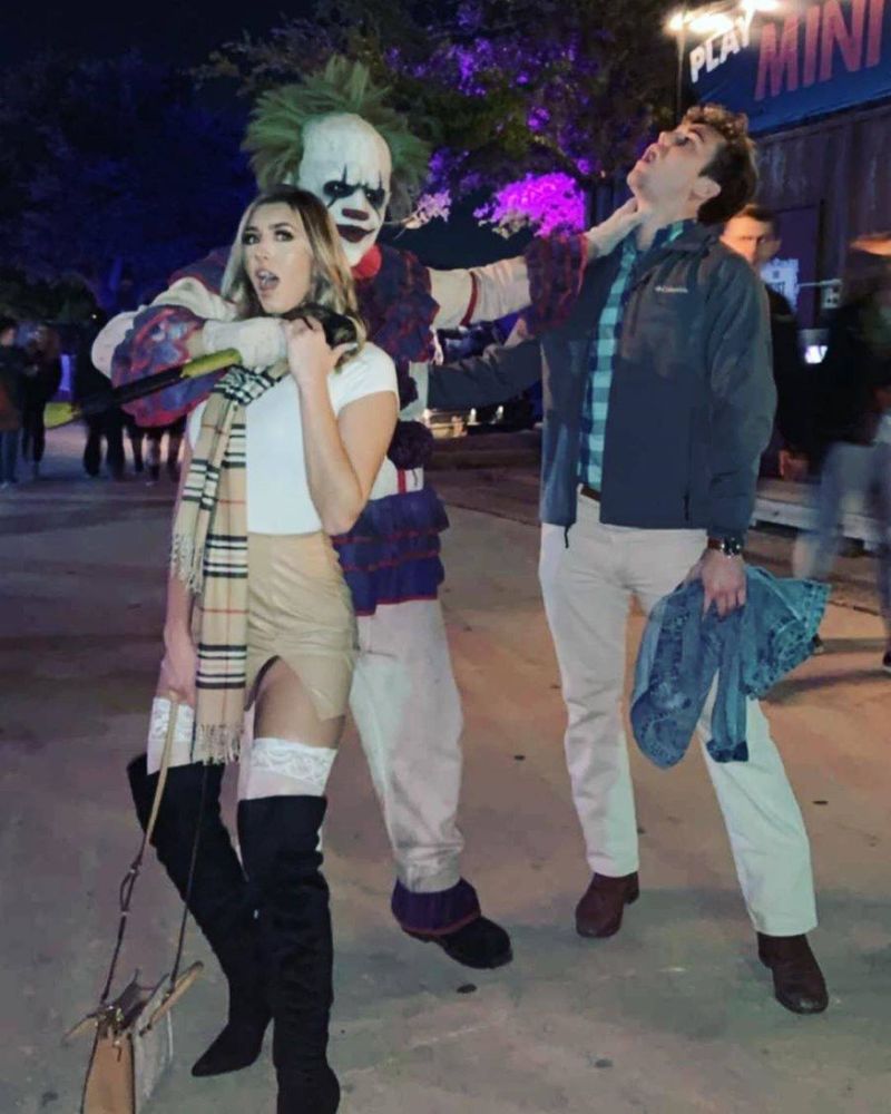A horror park clown strangles a couple, one with a rubber axe. 