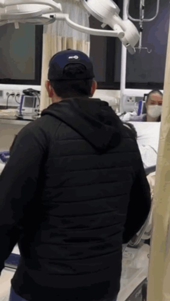 a man wearing a black jacket and a blue hat stands in a hospital