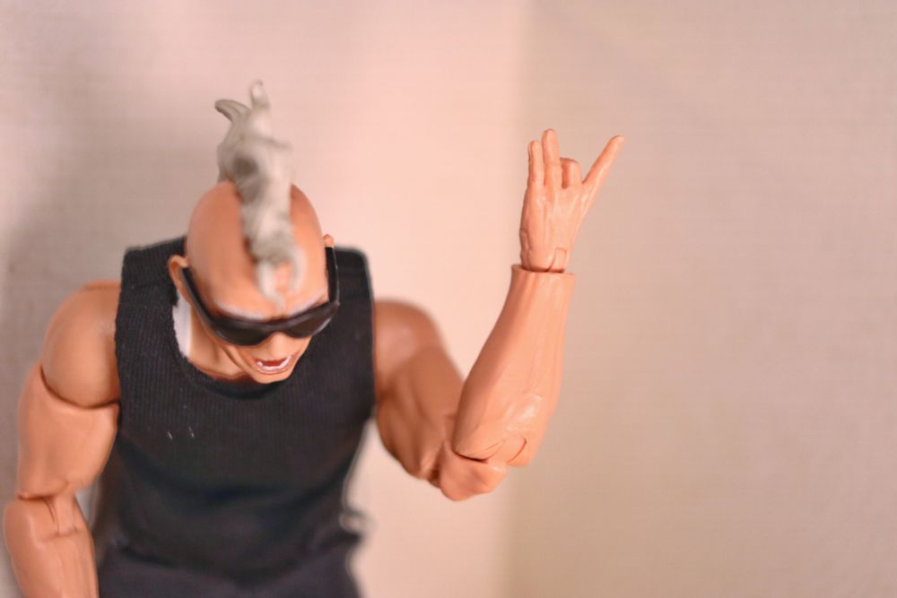 Action figure with their left hand raised. The first, third and pinkie finger are raised while the middle finger is bent  