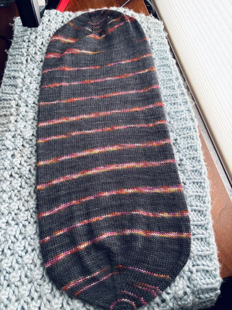 A 22” capsule of knit fabric in black and variegated stripes, which folds inward to form a double-layered hat 