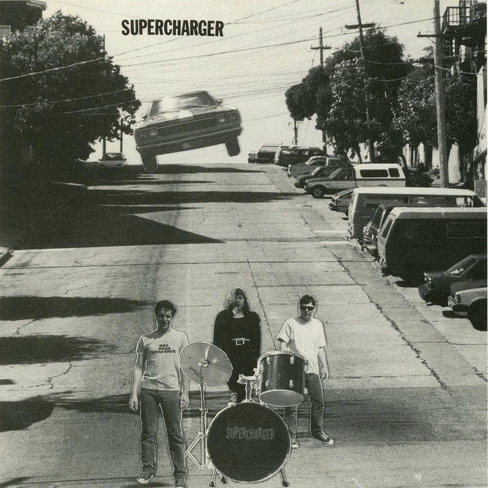 Cover of the first Supercharger record showing a collaged image of a car up on one side’s wheels coming down a San Francisco hill down towards the three members of the band 