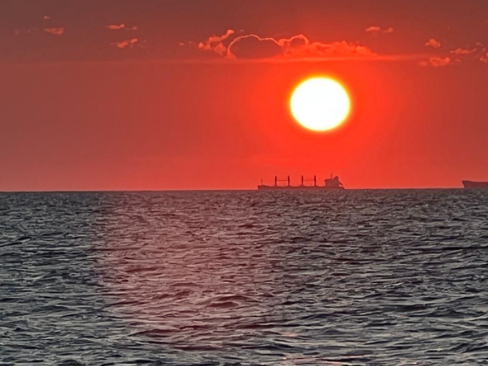Sunset on the Chesapeake Bay. The sky appears red and orange and the water appears black. A freight ship is on the horizon