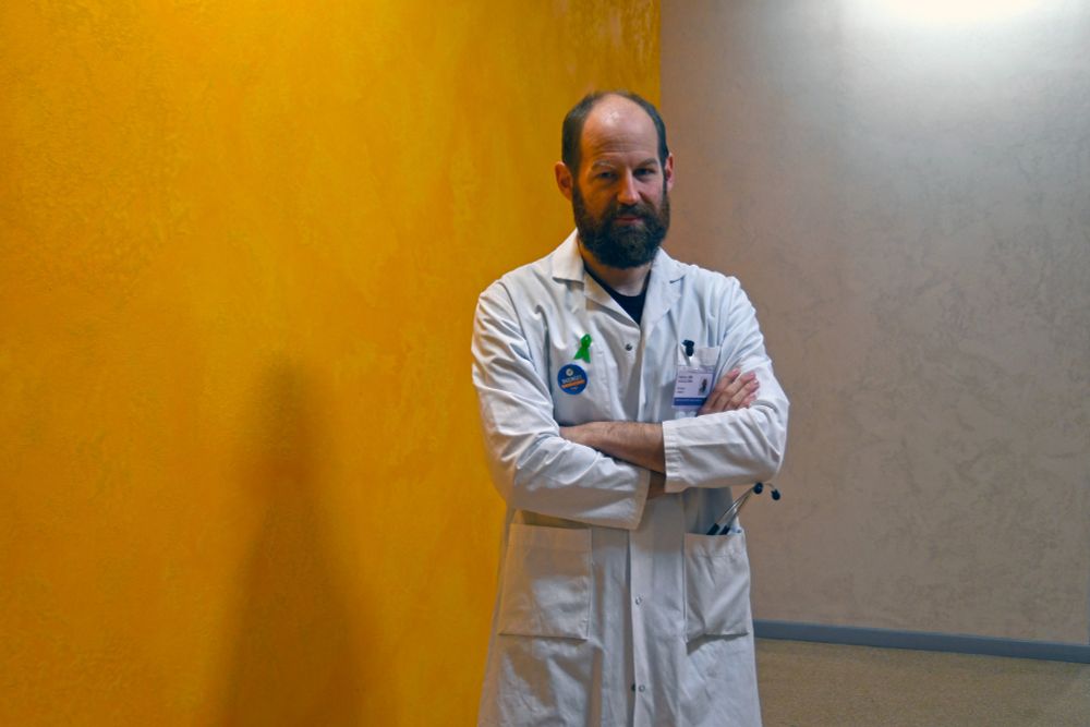Portrait du Dr Mickaël Bobot, en blouse blanche devant un mur coloré, bras croisés.