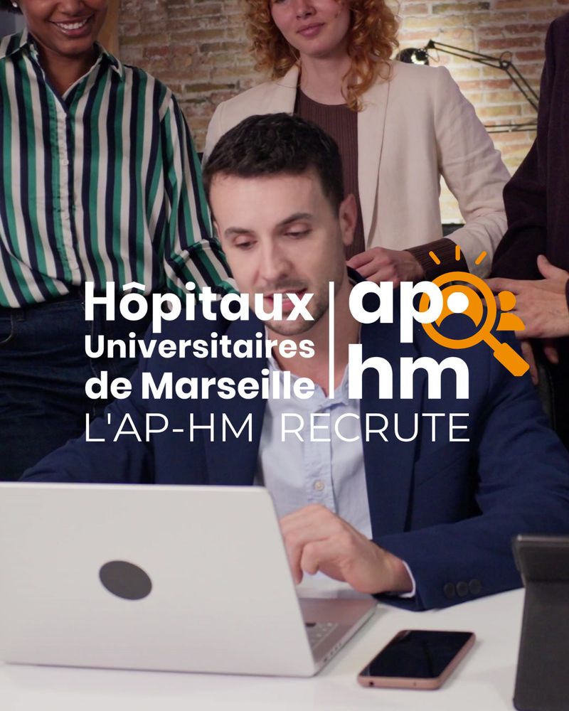 Un jeune homme en costume travaille sur un ordinateur portable entouré de collègues. En surimpression : logo de l’AP-HM et texte "L’AP-HM recrute".