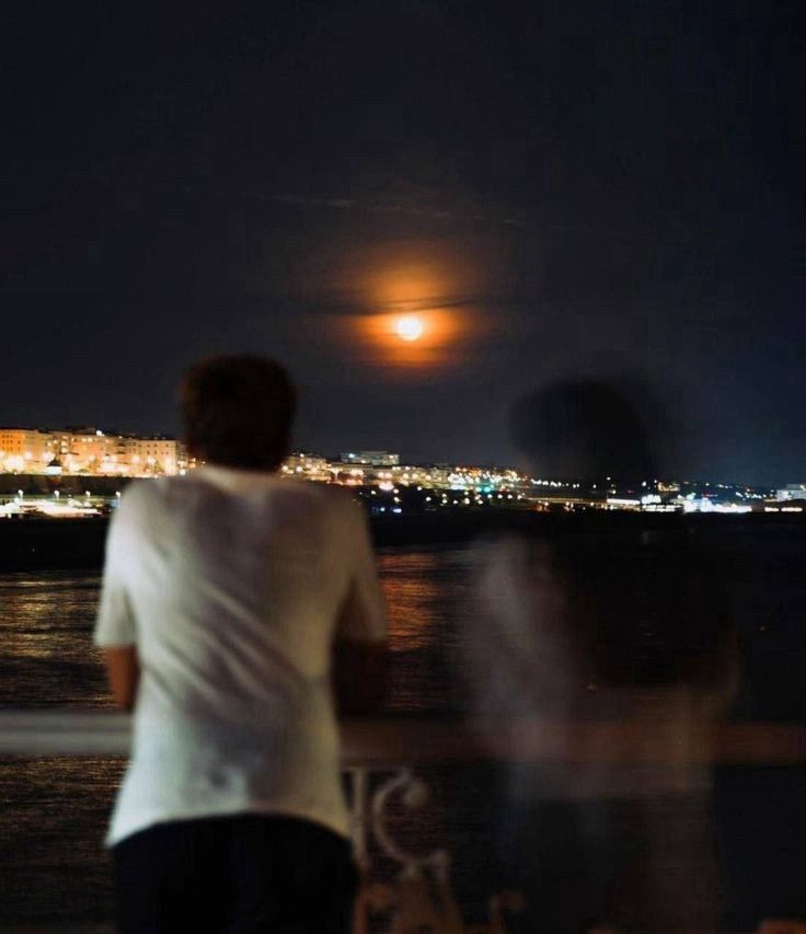 Two young men admiring a city nightscape. One of them is fading away, his image almost blending with the background.
