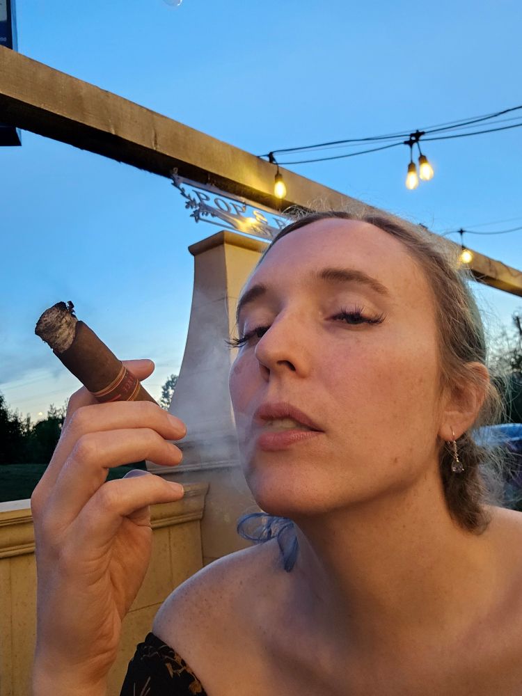Woman smoking a cigar with lights overhead and a blue sky in the background