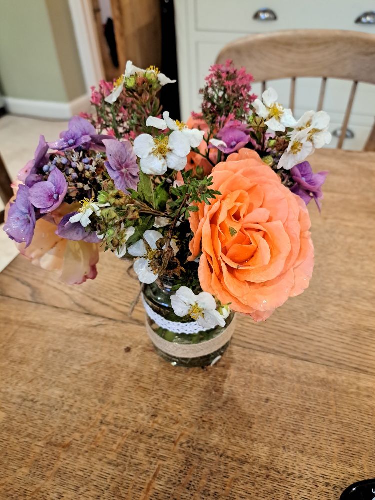 A posy of flowers in a glass jar on a wooden kitchen table