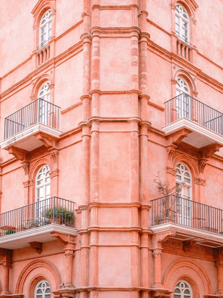 An exquisite example of classic Italian architecture, bathed in warm pink hues. This stunning facade in Umbria, Italy, features elegant balconies, ornate details, and arched windows that evoke a timeless charm. A perfect snapshot of the region's architectural beauty.