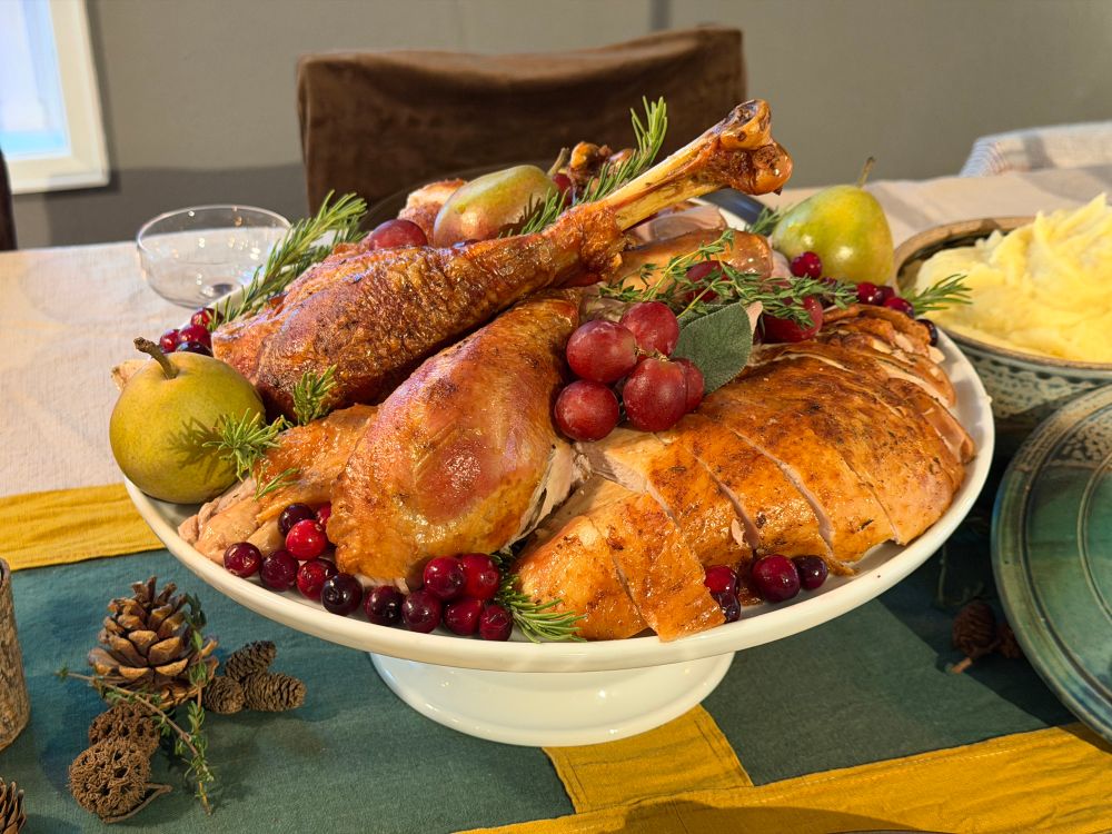 A display platter of carved turkey, grapes, cranberries, pears and herbs