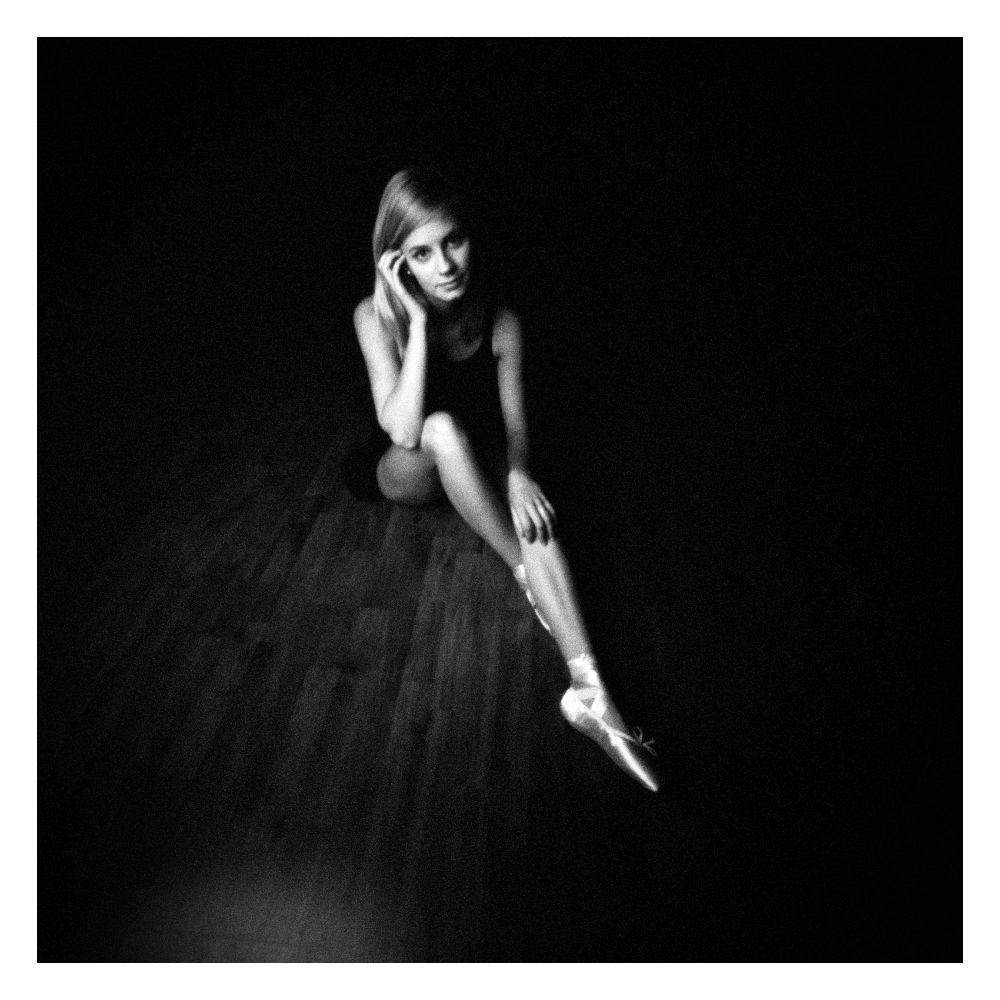 Sitzende Tänzerin auf Parkettboden.