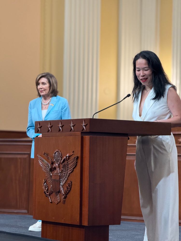 Elena Hung of Little Lobbyists speaks at a podium next to Speaker Emerita Nancy Pelosi