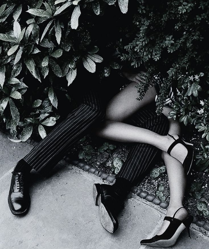 The image is a black and white photograph of an intimate moment / saucy shenanigans between two people, likely a couple or just people that are into shrubbery. They're partially obscured by foliage. 